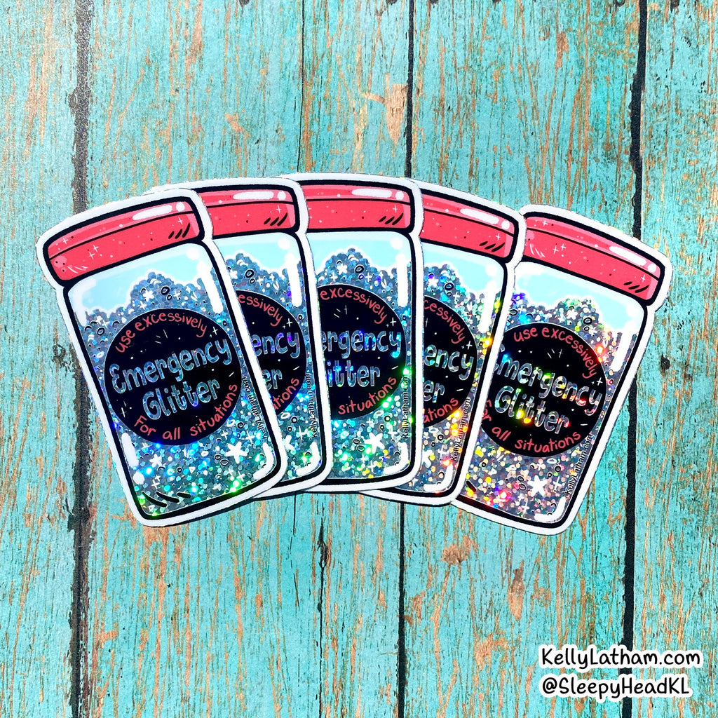 Four die-cut stickers of glitter jars arranged in a fan shape on a distressed turquoise wood background. The stickers depict clear jars filled with multicolor glitter, topped with pink lids, and labeled 'Emergency Glitter for all situations.