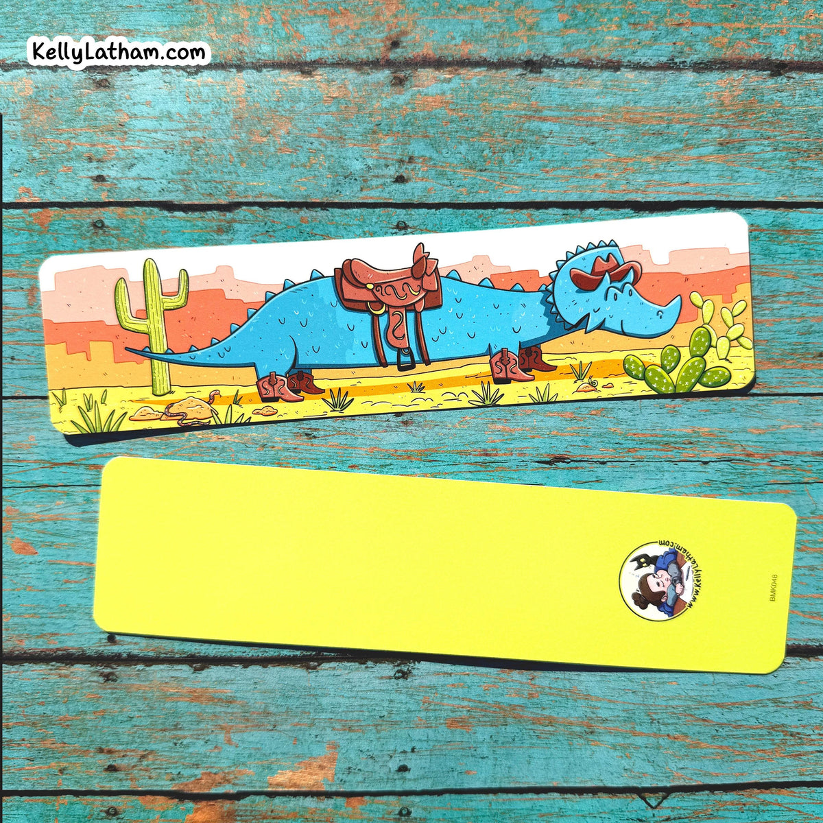 Two rectangular bookmarks distressed turquoise wood plank background. The top item features a colorful cartoon illustration of a blue dinosaur with a brown saddle in a desert scene, and the bottom item is a solid bright yellow rectangle with a small circular logo near the lower right.