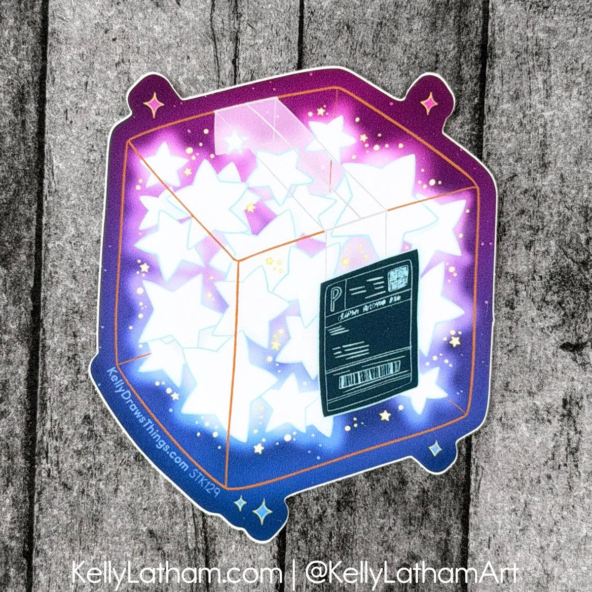 A die-cut sticker featuring a glowing 3D cube filled with white stars and a purple-to-blue gradient border, placed on a rustic gray wood background. A small black label on the sticker reads 'Pipkin Decorations' and 'Star Gazer Star'.