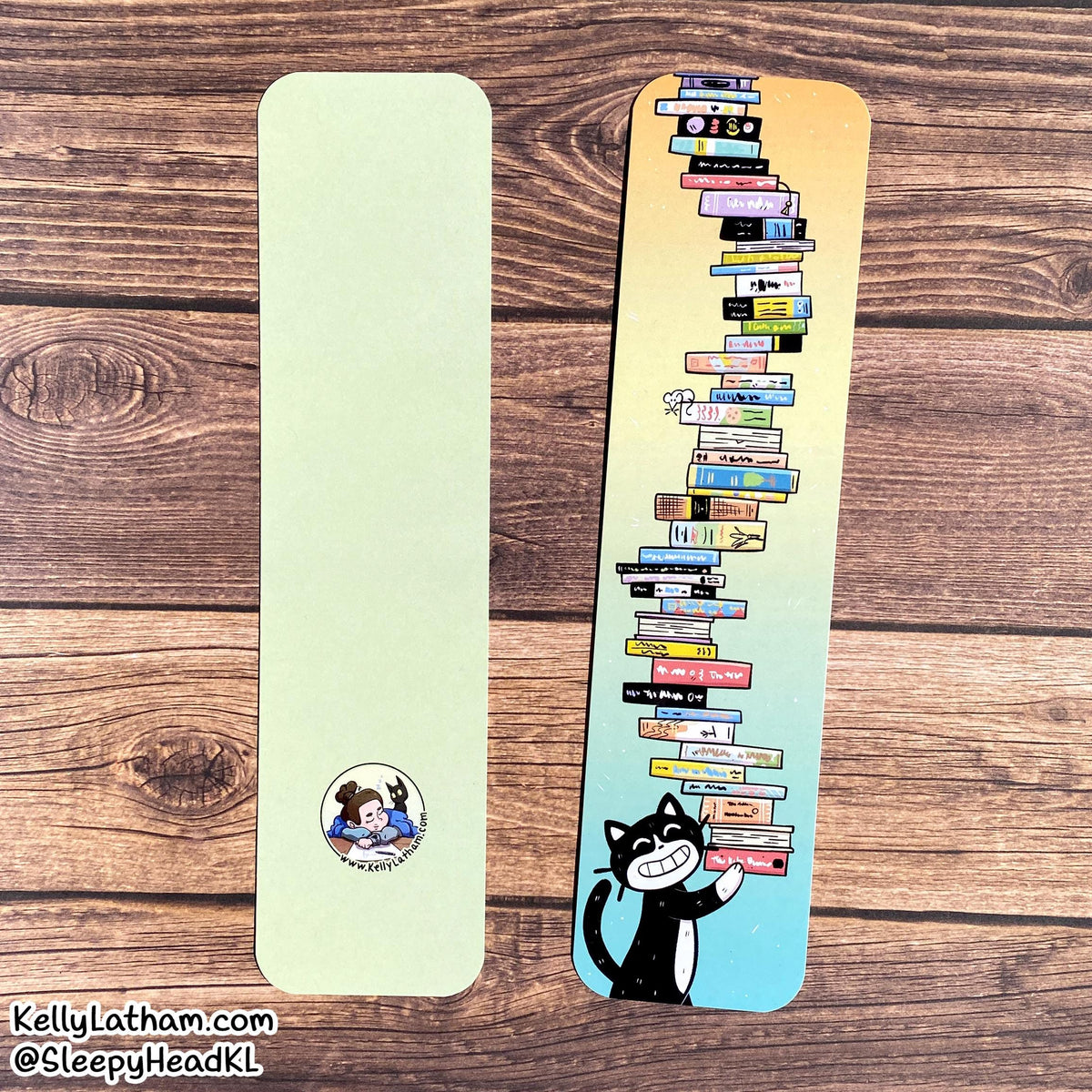 Two decorative bookmarks laid flat on a wood surface. One bookmark is plain pale yellow-green with a small circular character sticker near the bottom.