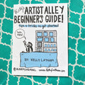 A printed card or booklet cover titled "Artist Alley Beginner's Guide!" with a cartoon illustration of a person waving in front of a building, placed on a teal patterned surface. Visible text includes "By Kelly Latham" and "@SleepyHeadKL www.