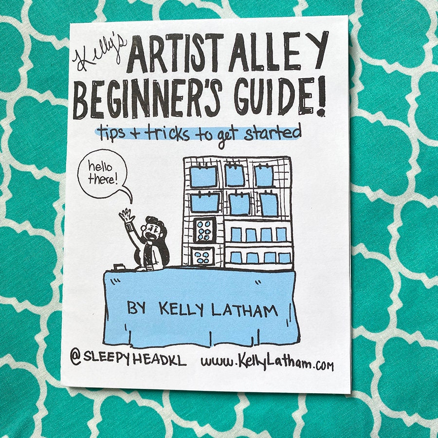 A printed card or booklet cover titled "Artist Alley Beginner's Guide!" with a cartoon illustration of a person waving in front of a building, placed on a teal patterned surface. Visible text includes "By Kelly Latham" and "@SleepyHeadKL www.