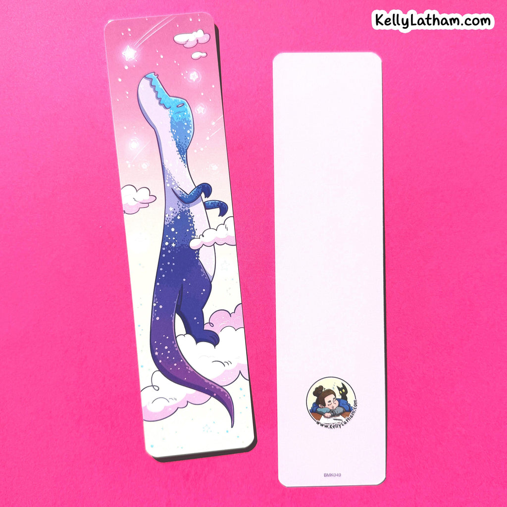 Two decorative bookmarks on a bright pink background. The left bookmark is printed with a whimsical illustration of a dinosaur in a starry blue and purple sky with clouds.