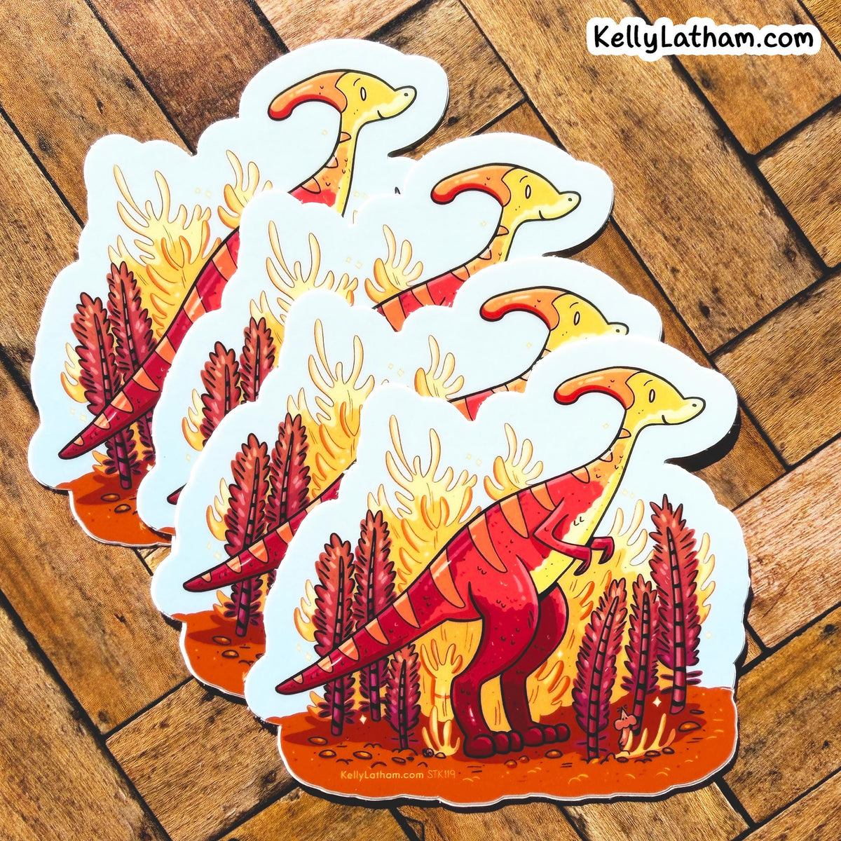 Four die-cut stickers featuring a cartoon red and yellow Parosaurus dino standing in orange flames with red plants, arranged on a wooden floor. The brand name KellyLatham.