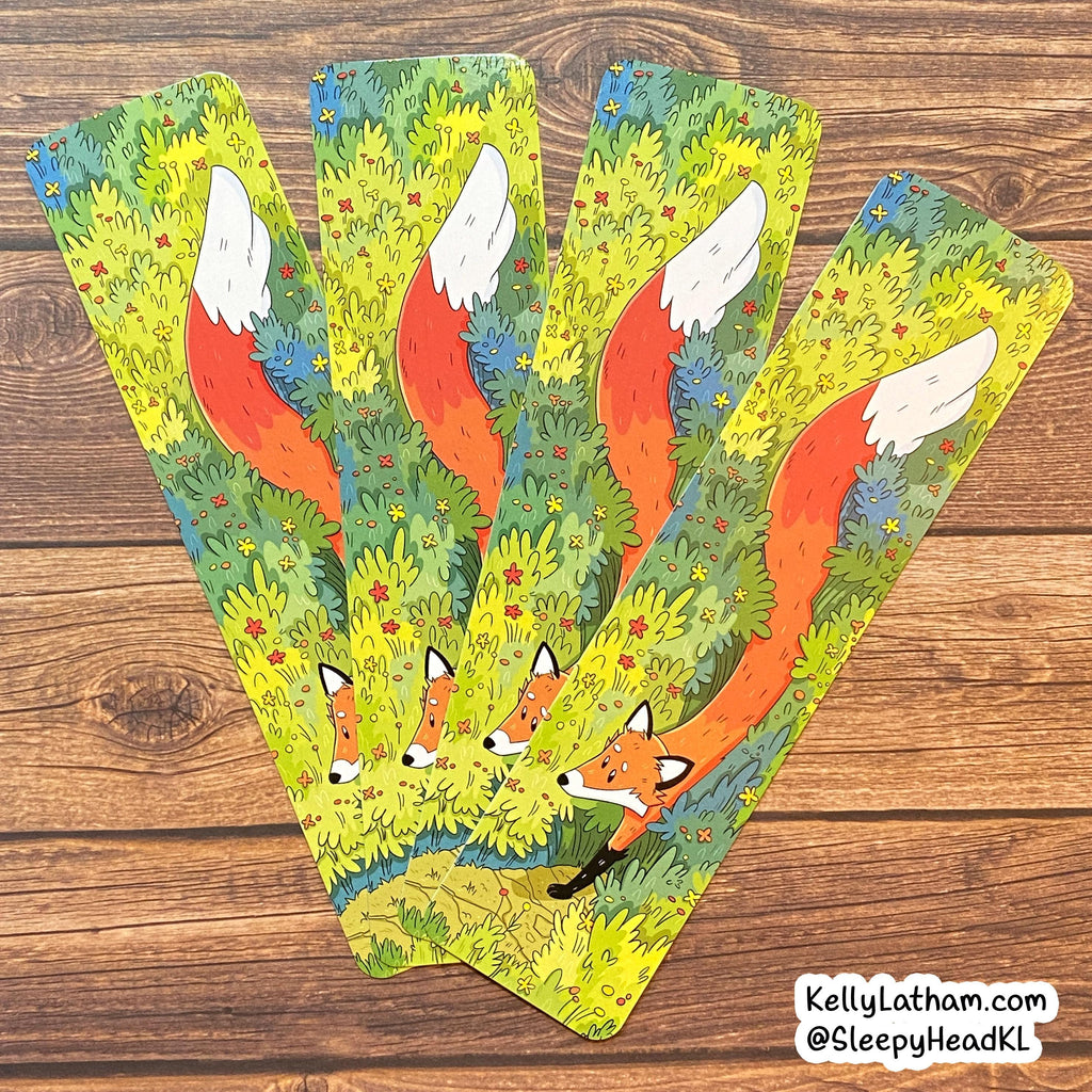 Four illustrated bookmarks fanned out on a wooden surface, featuring a whimsical forest scene with orange foxes, green and yellow foliage, and small blue and red details. A small watermark in the bottom right reads KellyLatham.