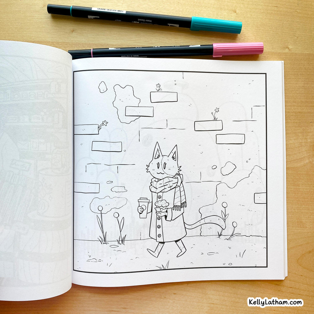 An open coloring book or art journal on a wooden surface, showing a black-and-white line drawing of a cat in a coat and scarf holding a cup. Two markers are placed across the top of the page.