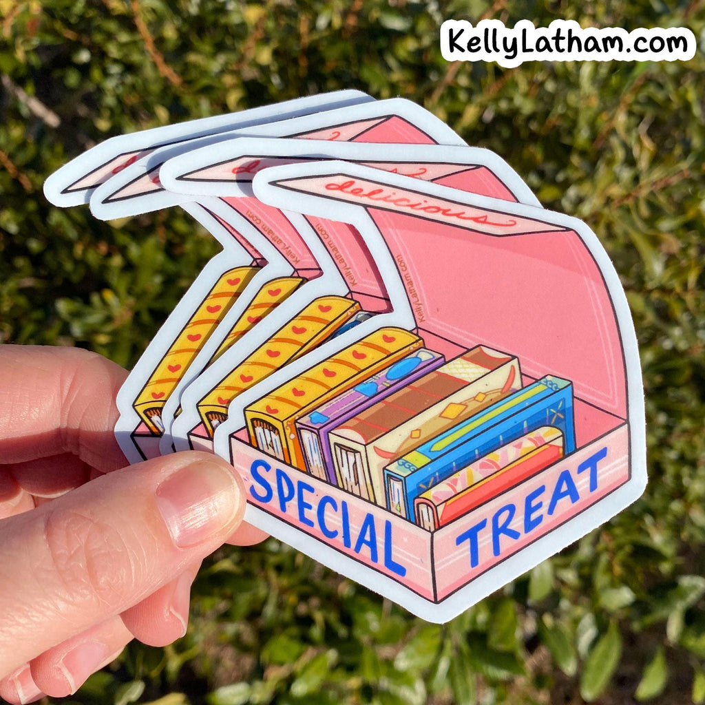 A hand holds a stack of die-cut stickers shaped like a pink candy box labeled 'SPECIAL TREAT,' with illustrated colorful candy bars inside. The background is blurred green foliage, and the text 'KellyLatham.