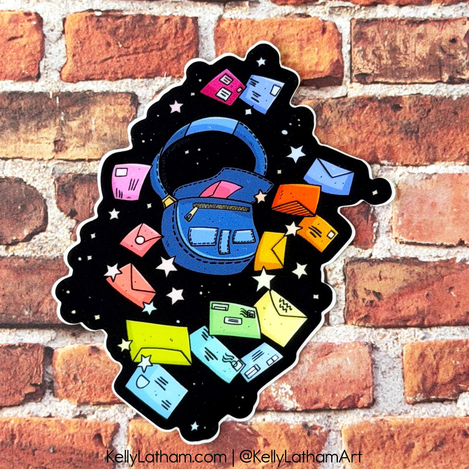 A die-cut sticker featuring a blue backpack on a black starry space background with colorful envelopes, shown against a red-brown brick wall. The sticker is branded with 'Kelly Latham' text at the bottom.