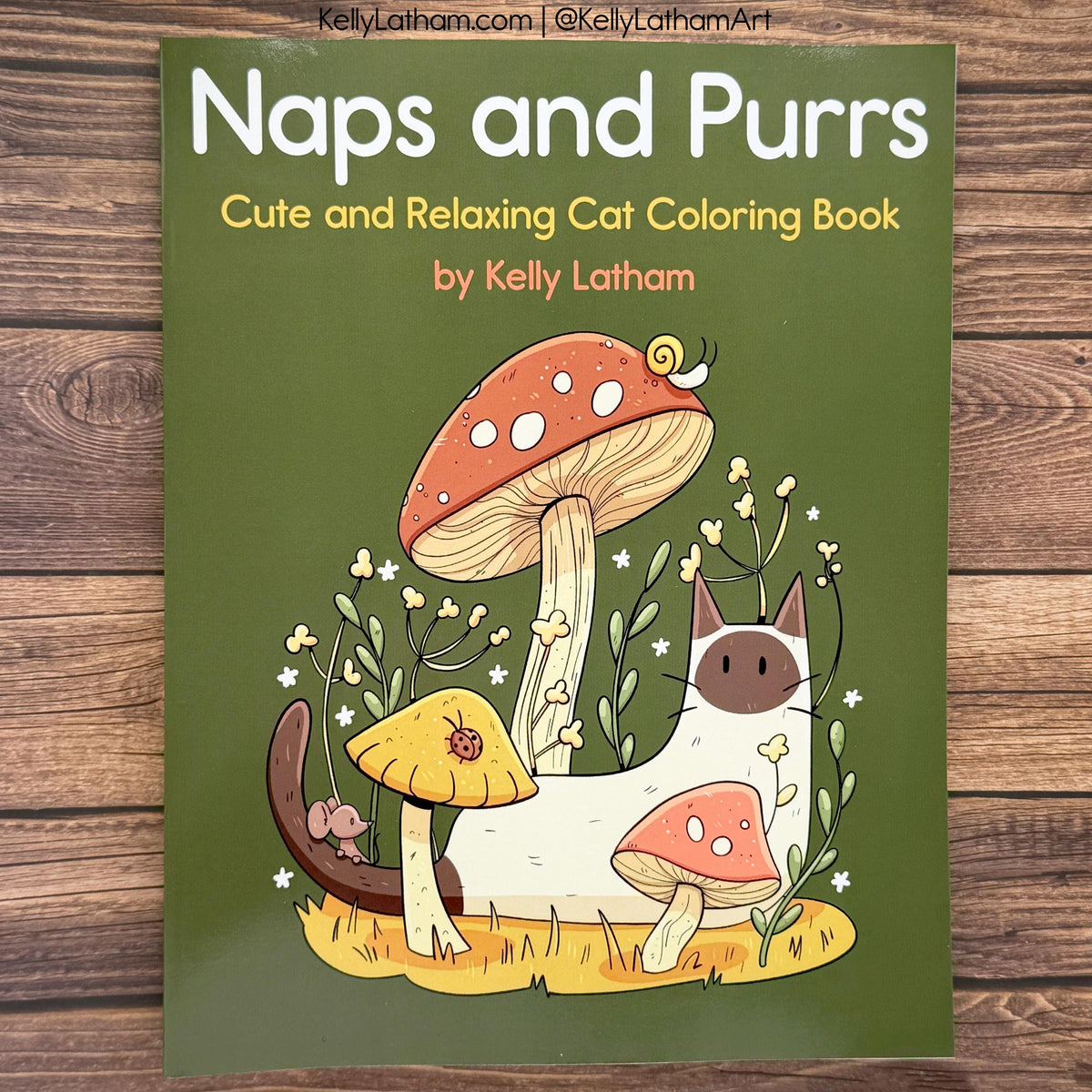 The front cover of the 'Naps and Purrs' coloring book by Kelly Latham, featuring a cute illustration of a white cat with a pink nose and a large red-and-white mushroom, placed on a wooden surface.