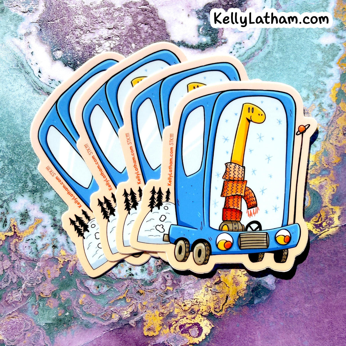 Four die-cut stickers featuring a whimsical blue bus carrying a long yellow giraffe wearing a knitted orange and red scarf, displayed on a colorful purple and teal marbled background. The brand name 'KellyLatham.