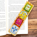 A colorful, hand-painted Thai wooden bookmark with intricate illustrations of a pink lotus flower, a green lotus leaf, and a yellow sun, displayed on an open book over a wooden surface.