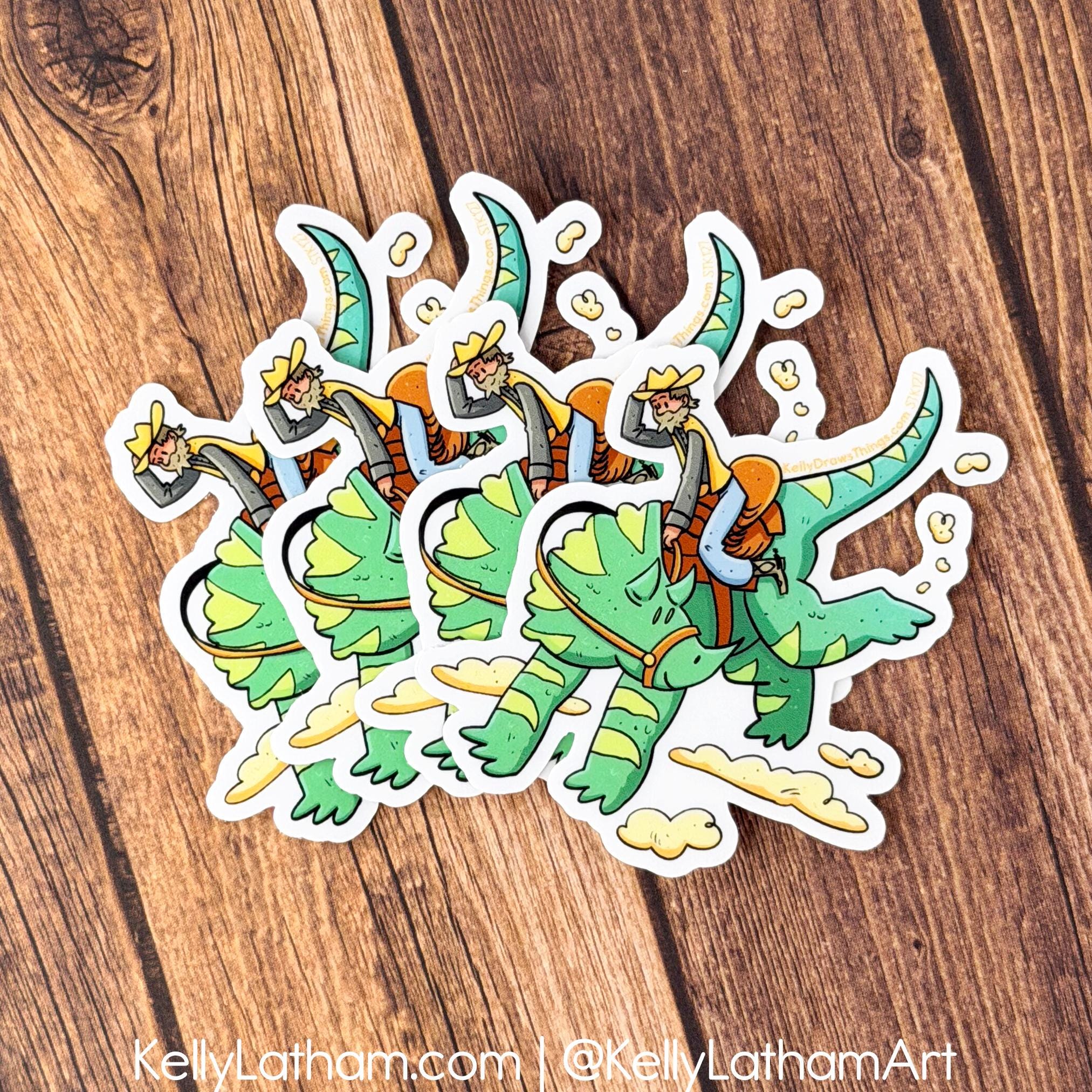 Colorful sticker of a dragon and riders on a wooden surface, with artist's name and website displayed.