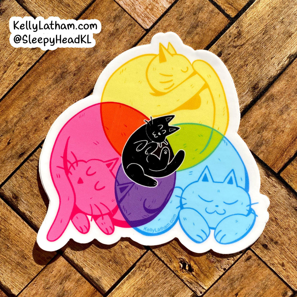 A die-cut sticker featuring four sleeping cats in pink, yellow, blue, and black, layered over overlapping translucent red, orange, green, and purple circles on a wooden floor background.