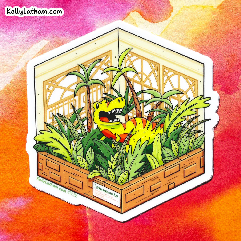 A die-cut sticker featuring a colorful cartoon illustration of a yellow T-Rex dinosaur surrounded by green palm trees and tropical plants inside a wooden crate, set against a vibrant orange and pink watercolor background. The sticker has a white border and the brand name 'KellyLathamArt' is visible on the label and in the top left corner.
