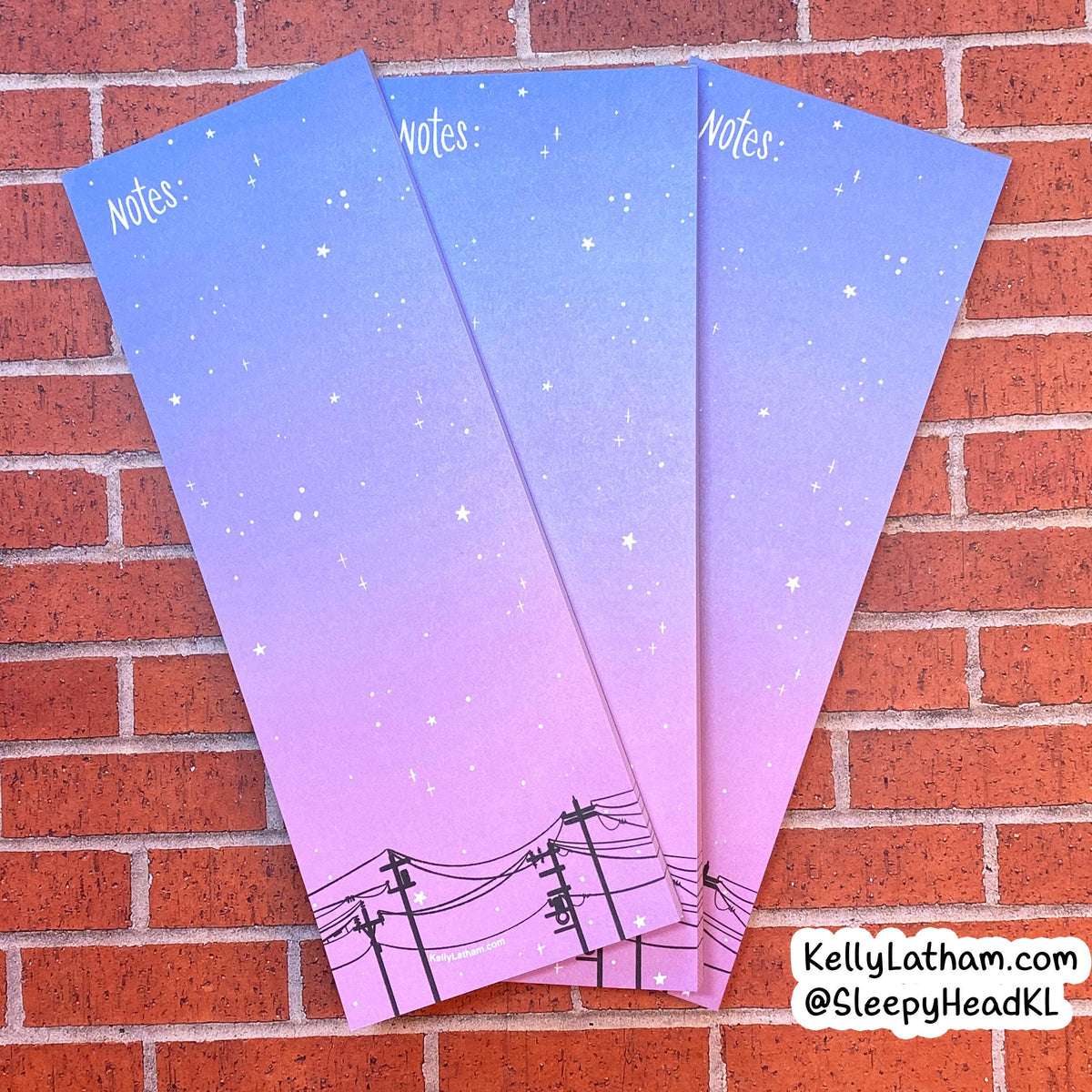 Three pastel gradient notepad sheets with a starry sky and power line design, fanned out on a red brick background.