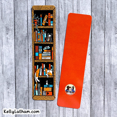 Two bookmarks shown on a gray wood plank background. One mat is illustrated with a bookshelf and books in warm brown, orange, blue, and black tones, while the second mat is solid bright orange with a small circular logo near the bottom.