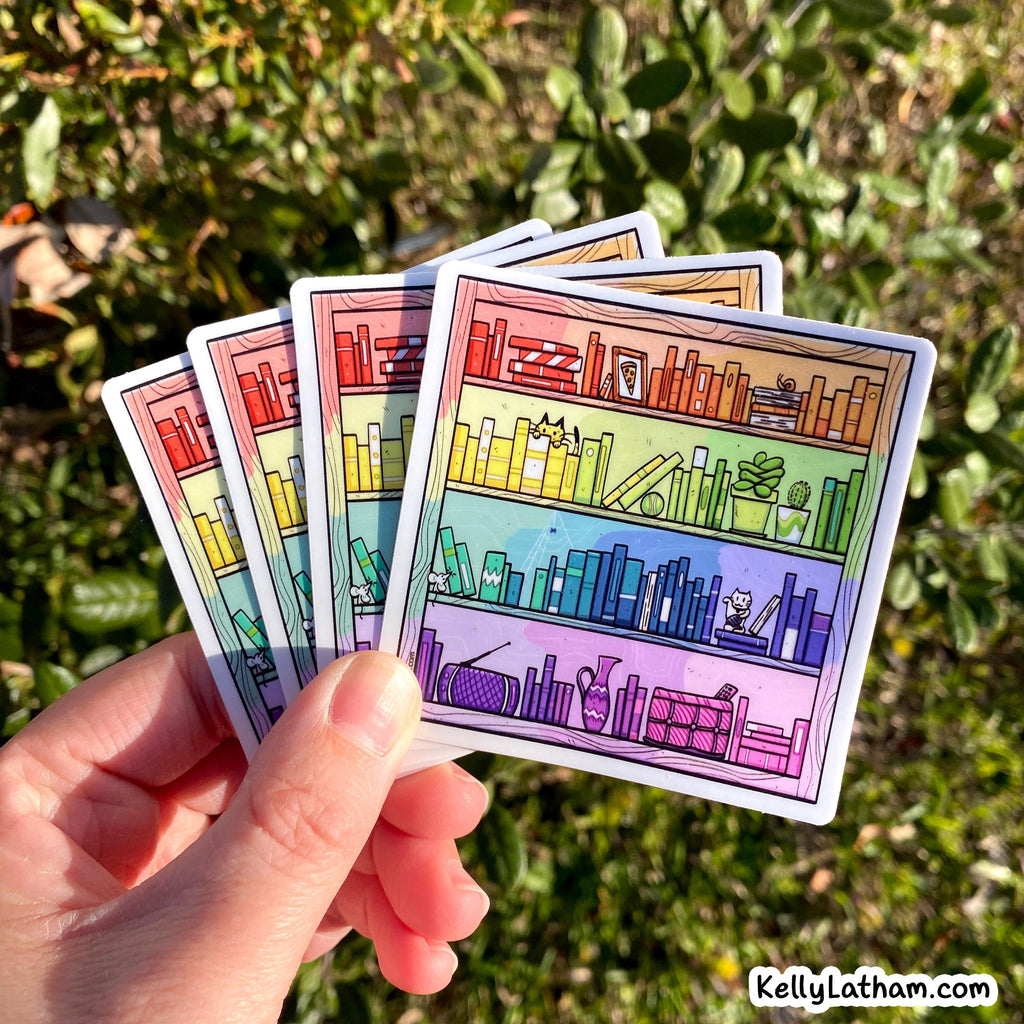 A hand holds four illustrated bookshelf stickers outdoors against a blurred green garden background. The stickers show colorful rainbow shelves with books and small decorative items.